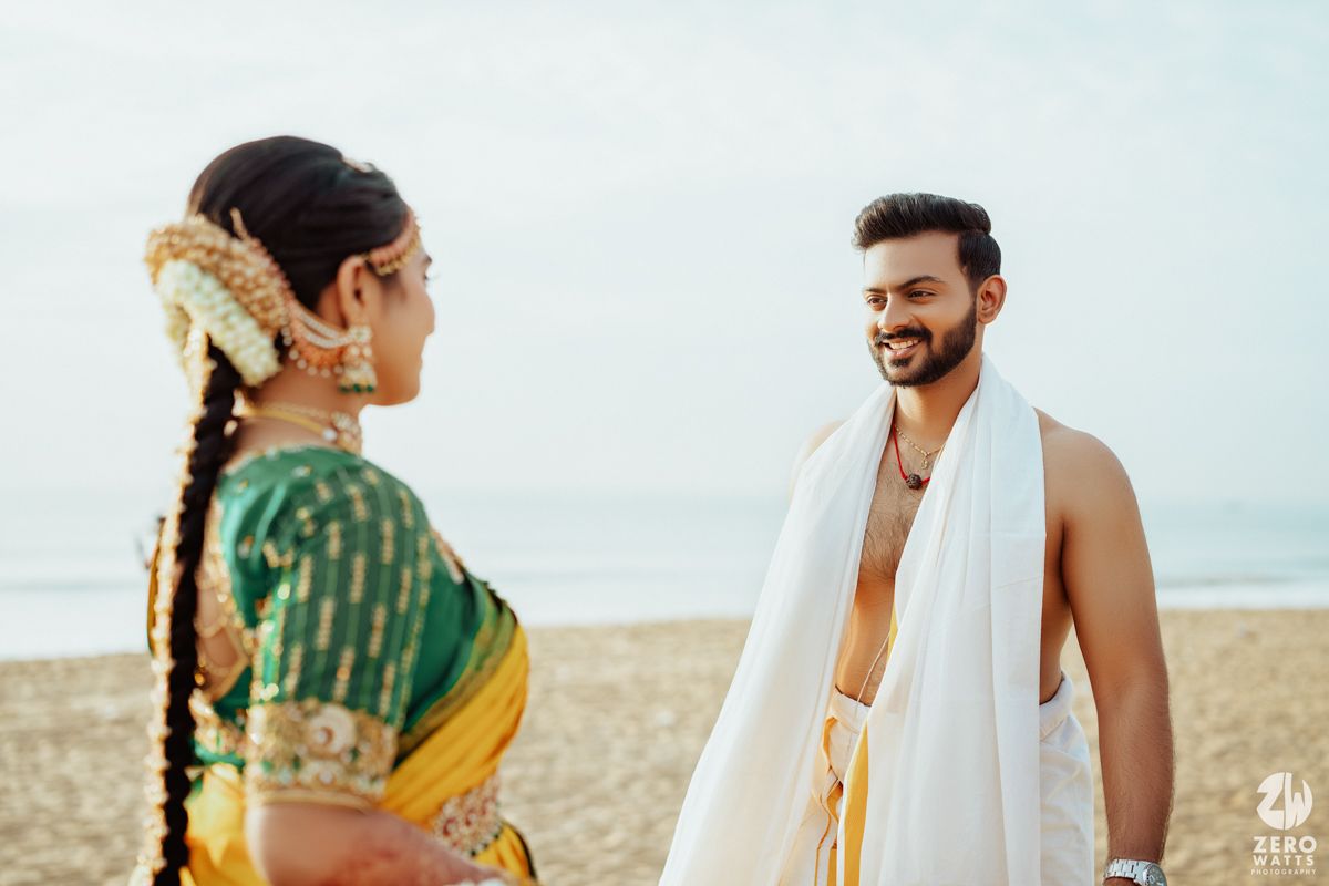 Candid shot of South Indian couple in traditional wedding attire on beach.