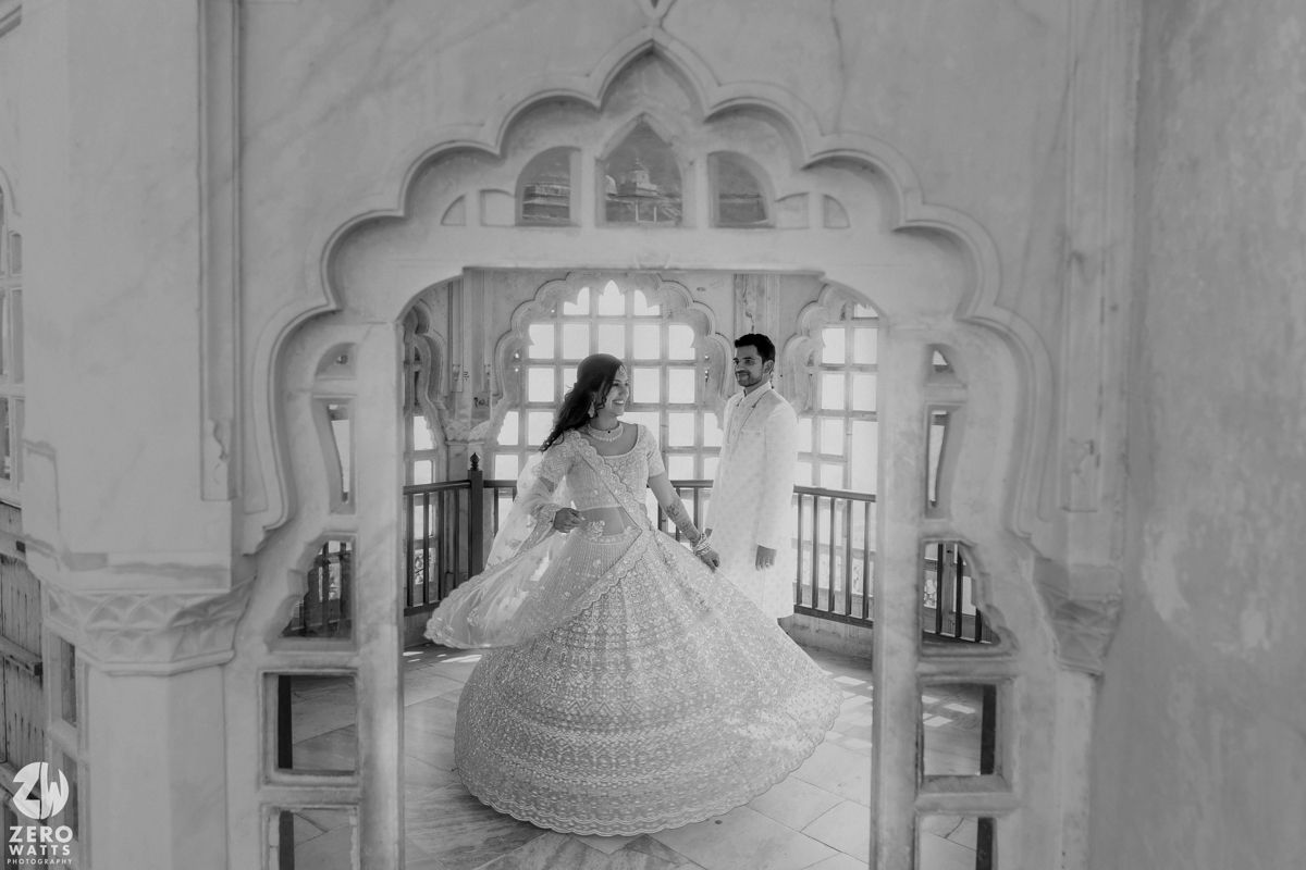 Wedding couple poses under elegant white stone archway in black and white photograph.