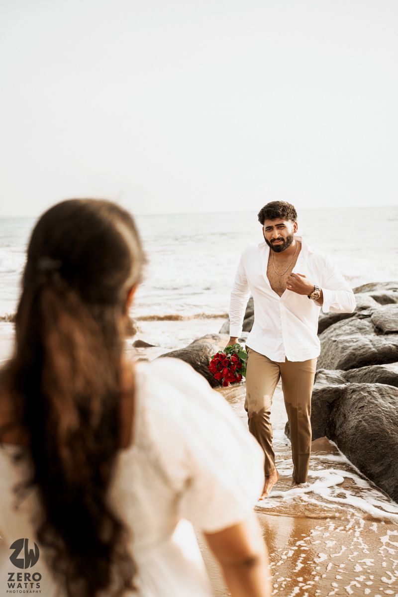 A beachside photoshoot with two people in white outfits navigating rocky terrain.