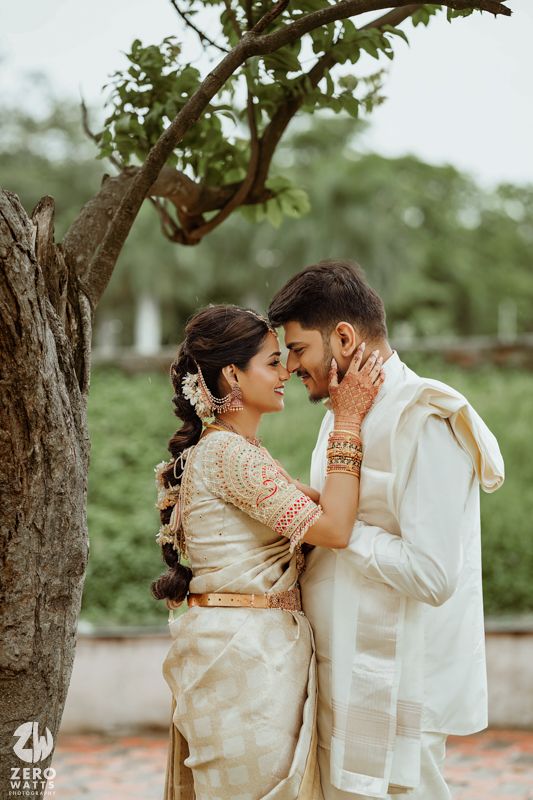 Wedding couple in cream and gold Indian attire share candid moments against a green outdoor backdrop.