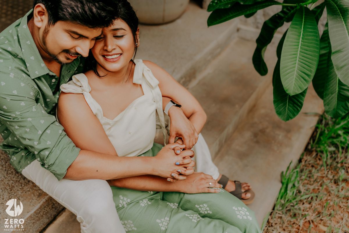 A tender moment captured during a garden wedding photoshoot with a couple embracing under lush green foliage.