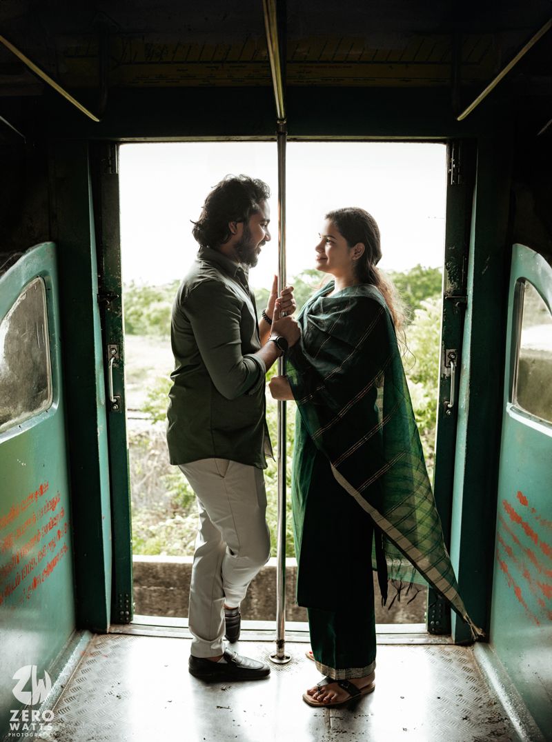 A romantic moment captured between a couple standing in the doorway of a moving train with scenic backdrop.