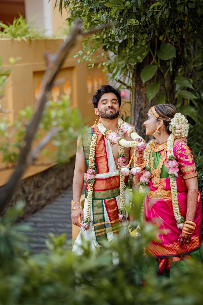 Newlyweds in traditional South Indian wedding attire pose together in a lush garden setting.