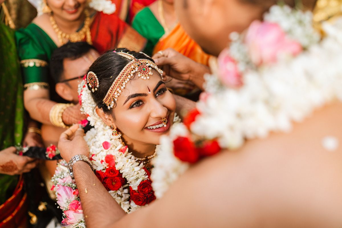 Smiling guest wearing traditional Indian bridal jewelry and floral garlands during a wedding ceremony.
