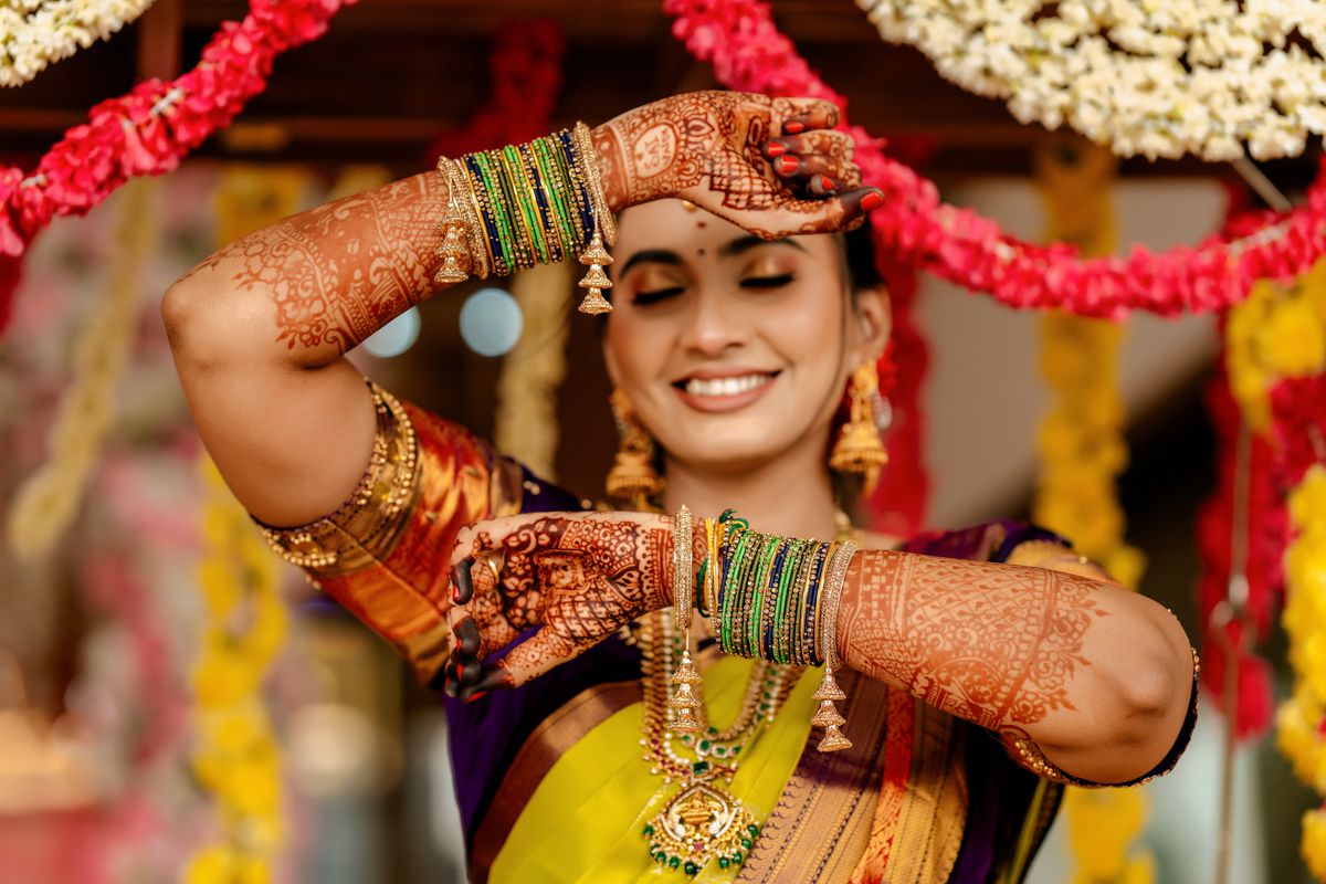 Traditional Indian bride wearing yellow saree and bangles shows off intricate henna designs on her hands during celebration.