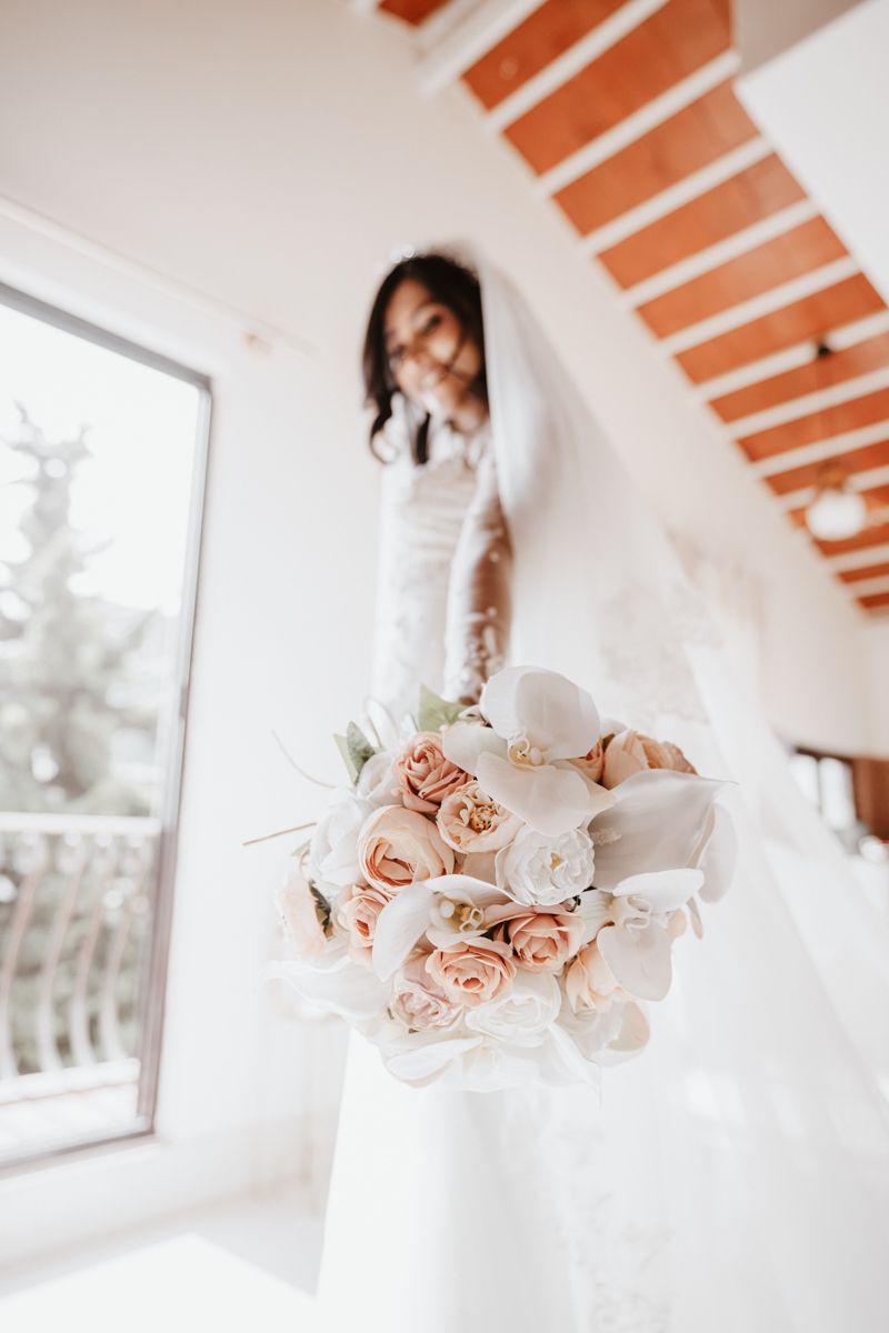 A delicate bridal bouquet of blush pink and white roses held against a bright white interior.