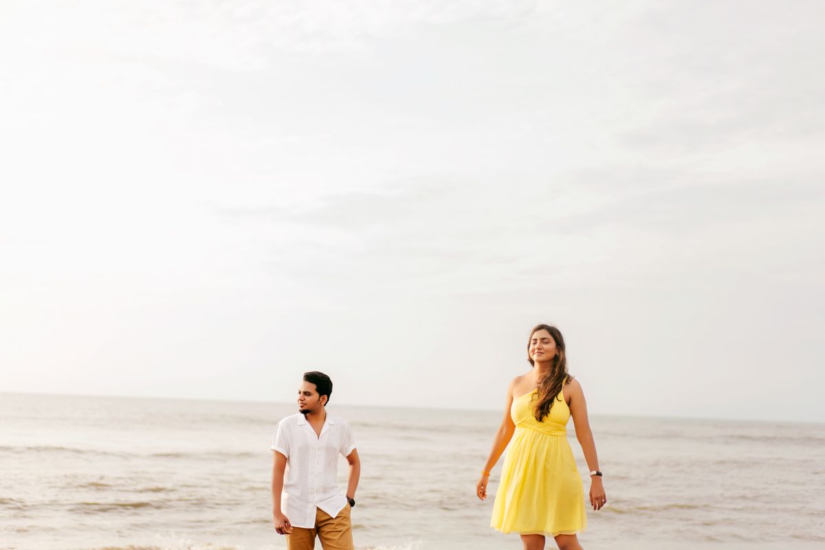 Couple in summer attire walking along empty beach during golden hour.