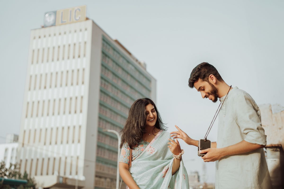 A couple shares a joyful moment while standing near a modern office building on a bright day.