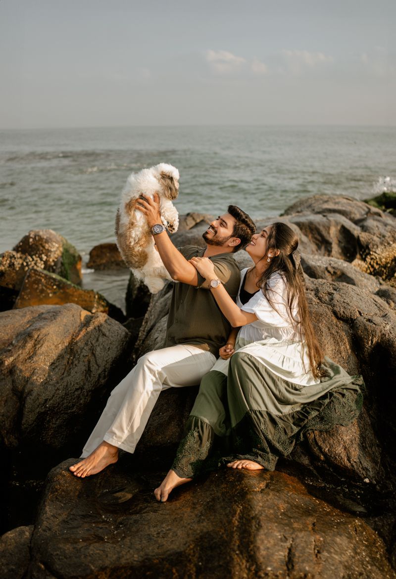 Couple playing with white dog on coastal rocks by the ocean.