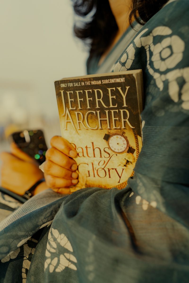 Close-up shot of Jeffrey Archer book 'Paths of Glory' held against blue floral patterned dress.