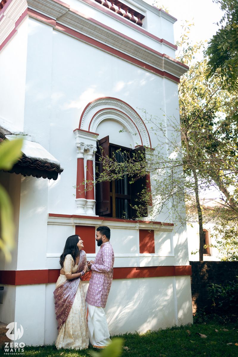 A couple stands together near the arched entrance of a white colonial-style building with red trim details.