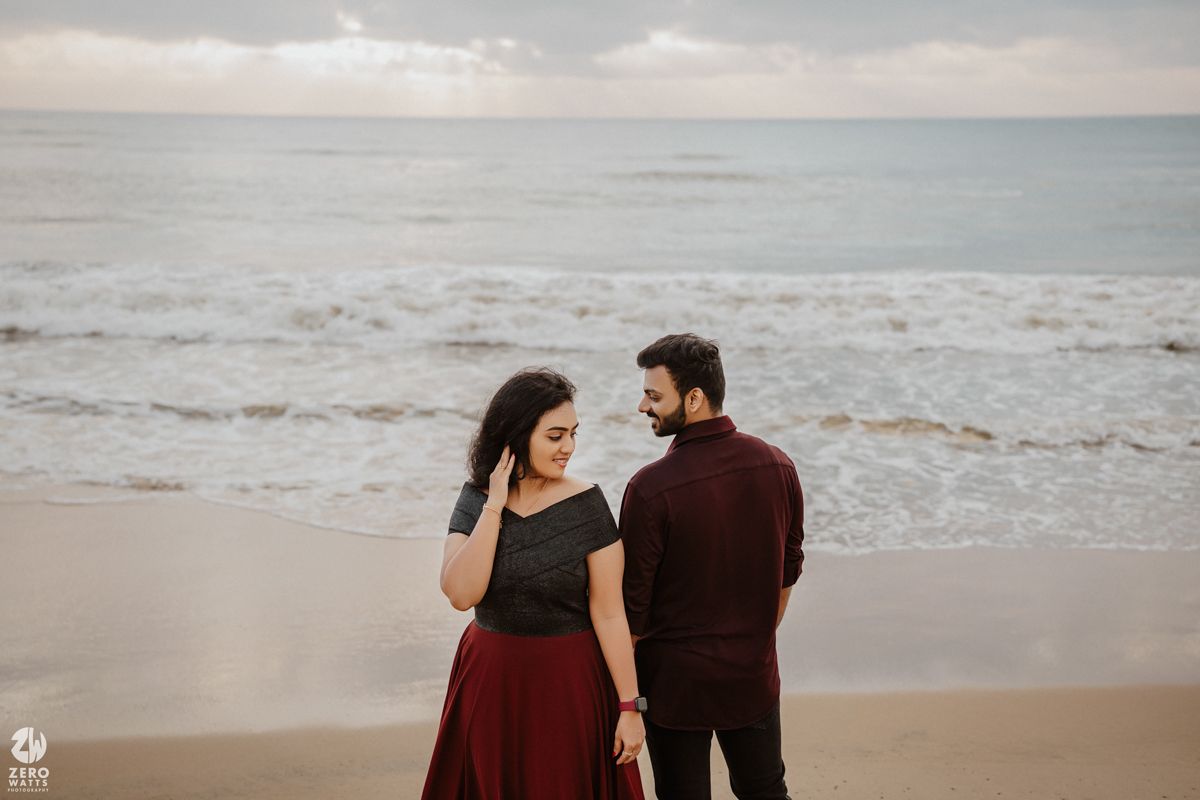 Couple in dark attire walking together on a misty beach during overcast weather.