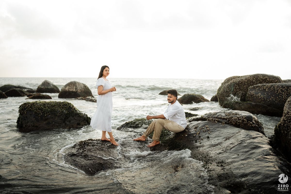 Romantic beach proposal scene on rocky coastal shoreline during sunset.