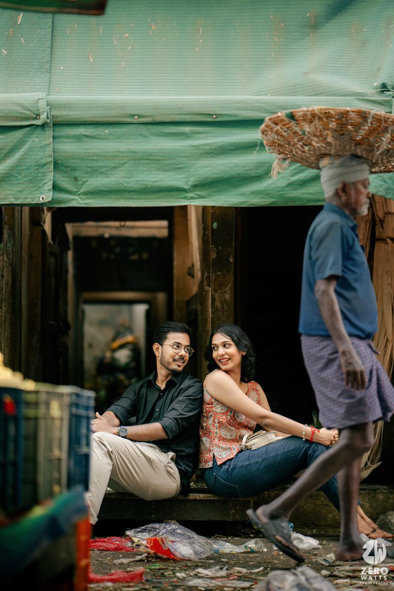 Couple share a happy moment sitting under green canopy as person walks past.