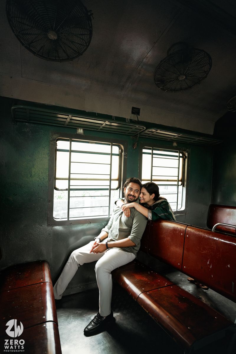 A couple sharing a tender moment on wooden seats inside an old train car with ceiling fans visible.