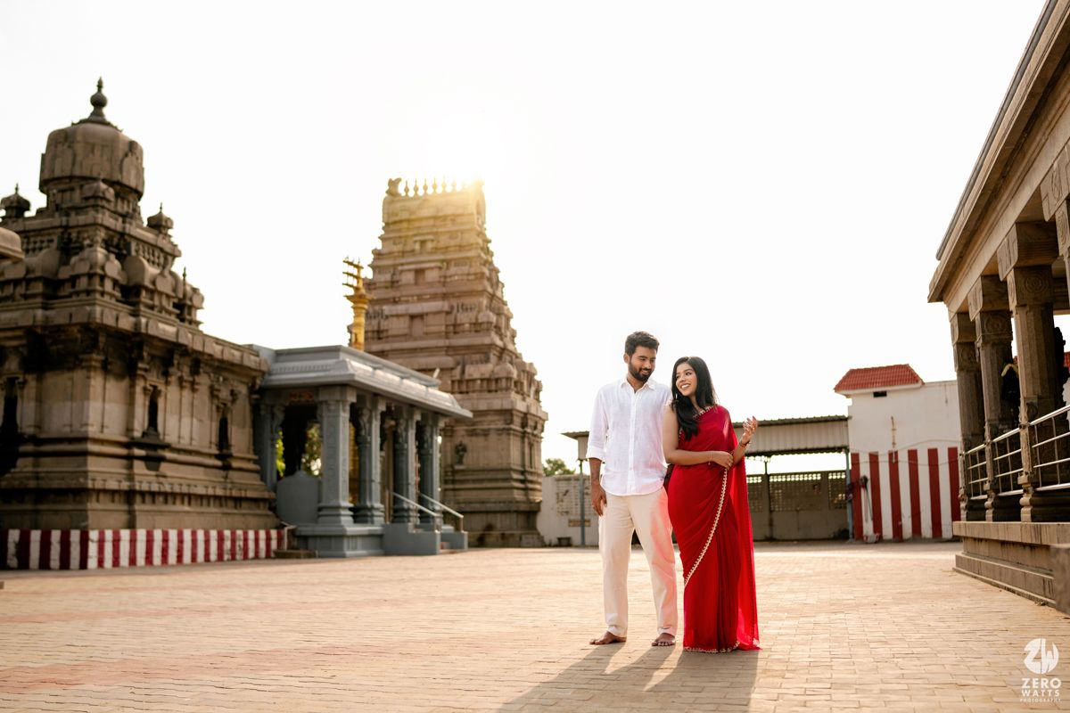 A couple walks along the ornate architecture of a temple complex in India, showcasing ancient stone structures and pillars.