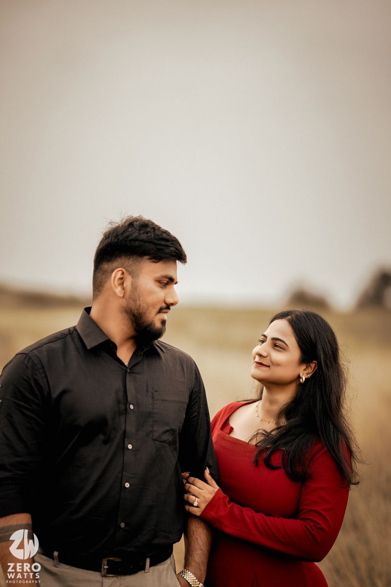 Couple in red and black outfits sharing a romantic moment in a field.