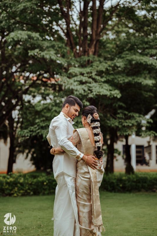 Couple in traditional attire dancing playfully on a green lawn with trees in the background.