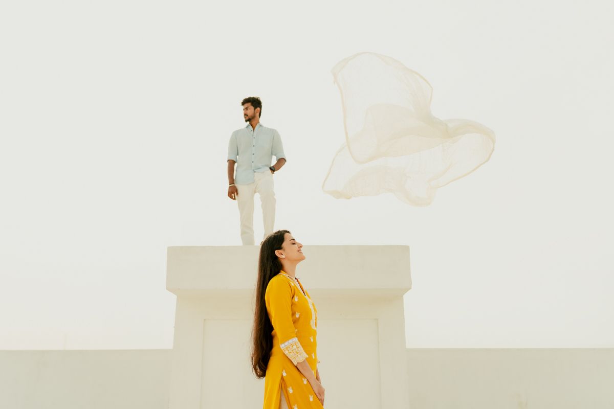 Two people create artistic poses against a white architectural backdrop, with one in yellow and one in white.