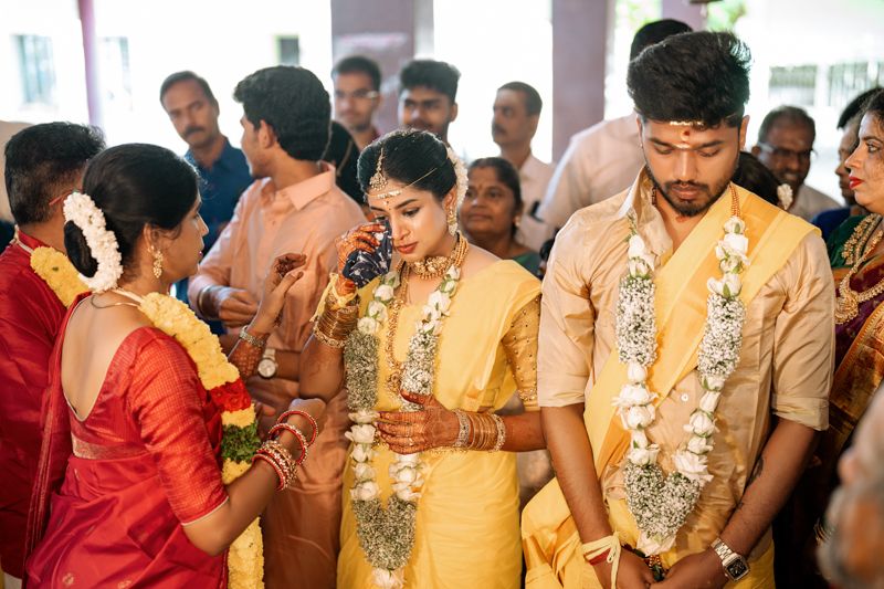People in traditional yellow and red attire participate in a cultural ceremony, adorned with flower garlands.