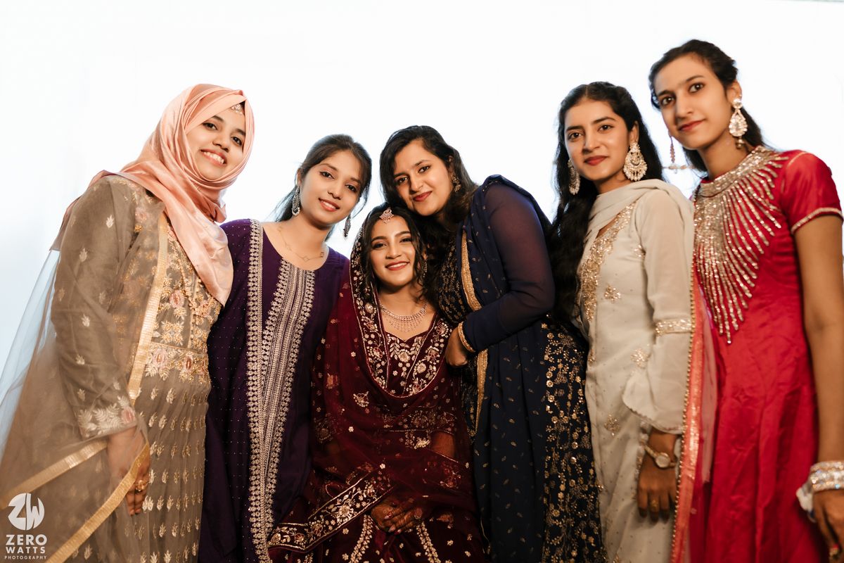 Group of women in colorful traditional South Asian attire posing together at a celebration.