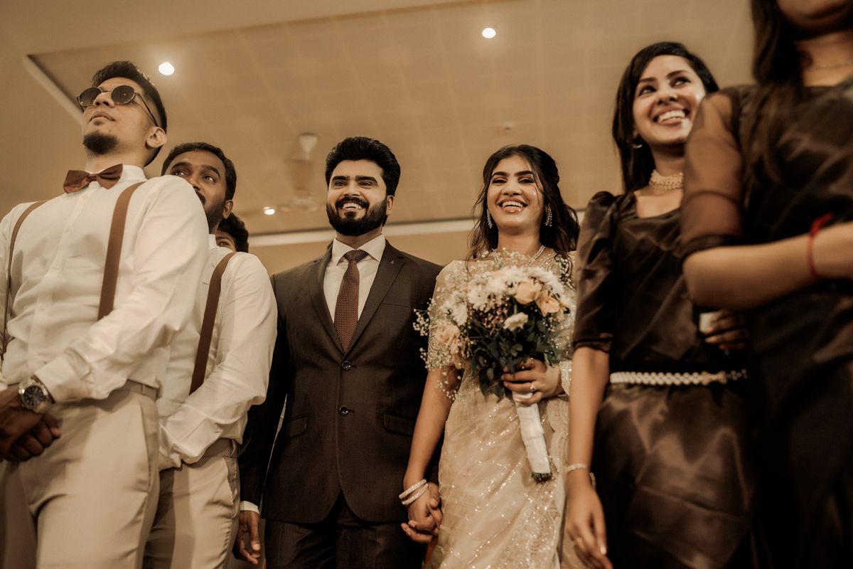 Wedding party laughs together during a candid moment at reception with warm sepia lighting.