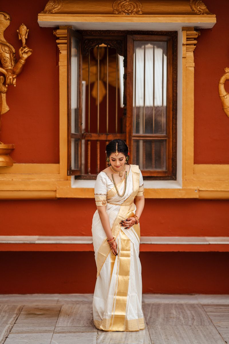 Traditional South Indian attire on display against a rustic red wall with ornate window and golden decorative elements.