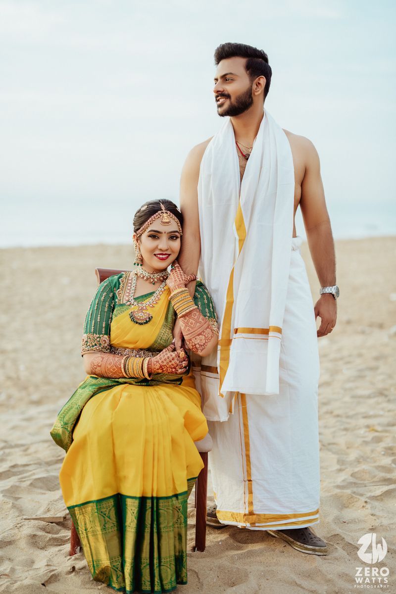 South Indian couple in traditional wedding attire pose together on sandy beach for outdoor photoshoot.