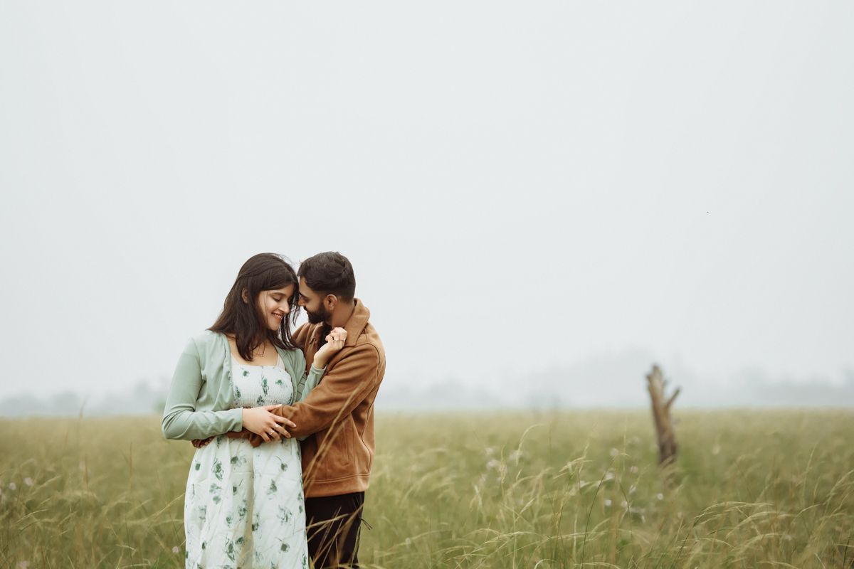 A couple shares an intimate moment while standing together in a misty field with tall grass.