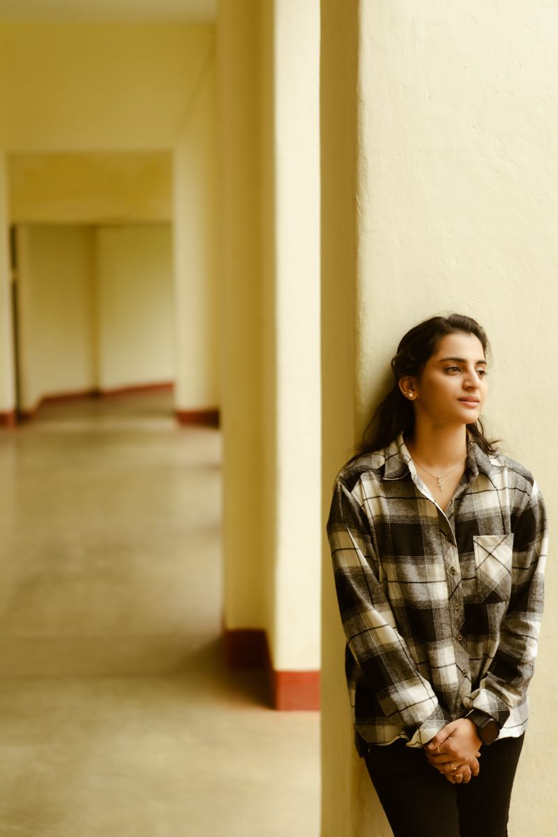 A person in a plaid flannel shirt stands contemplatively in a long hallway with yellow walls and maroon trim.