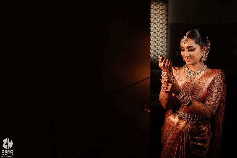 Traditional Indian bride wearing silk saree and jewelry holds a decorative light against dark background.