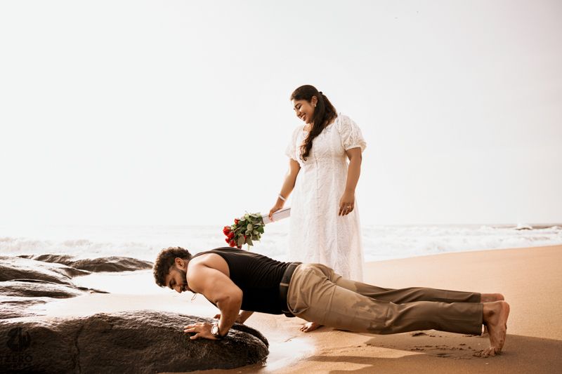 Playful beach photoshoot moment with couple on rocky shoreline.