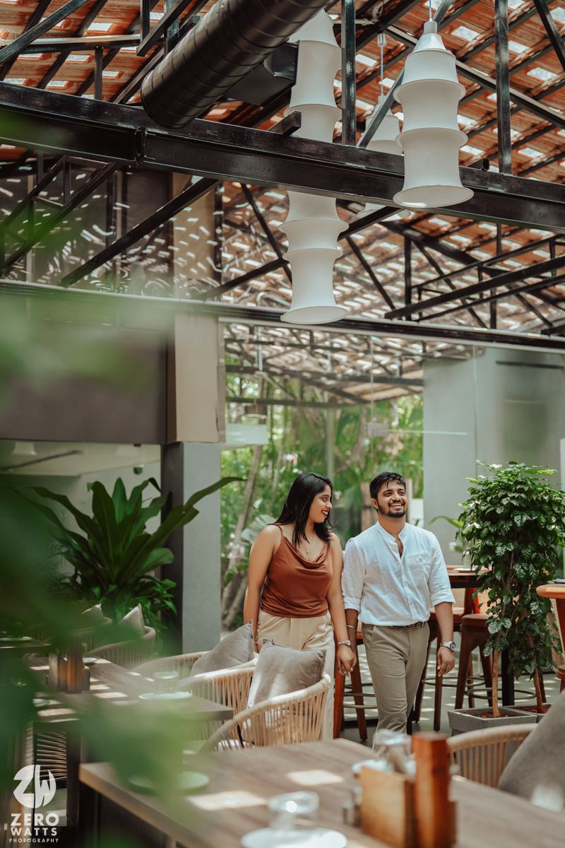 Couple enjoying a romantic moment in a greenhouse-style restaurant with tropical plants and wooden decor.