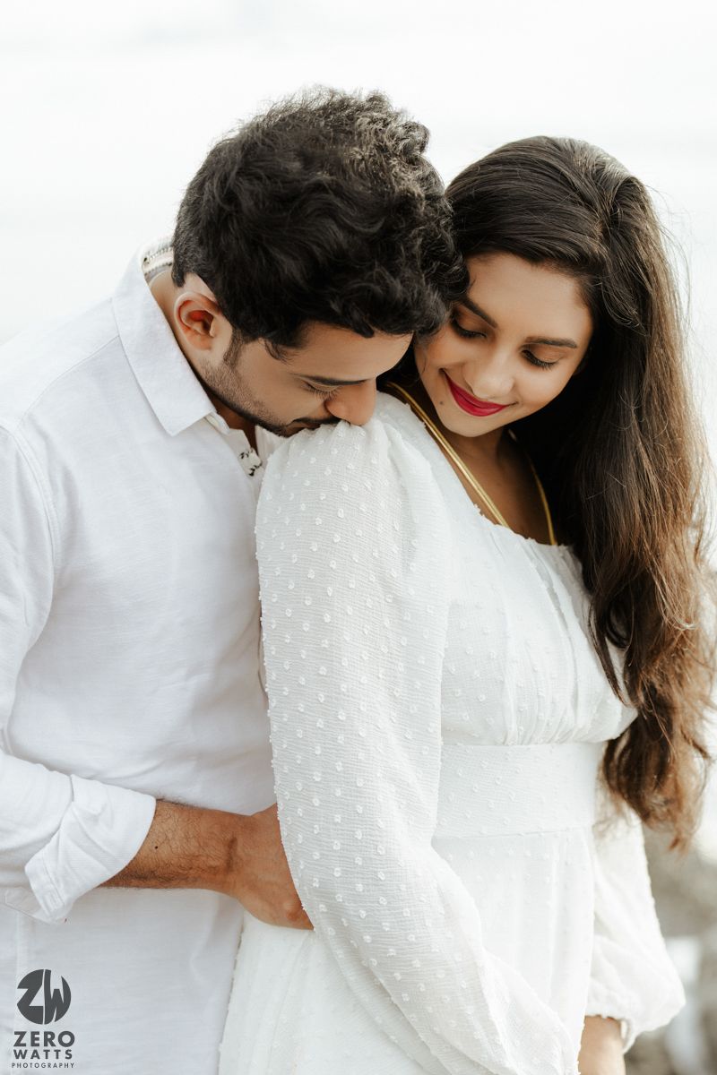 Romantic couple in white outfits share an intimate moment against a bright background.