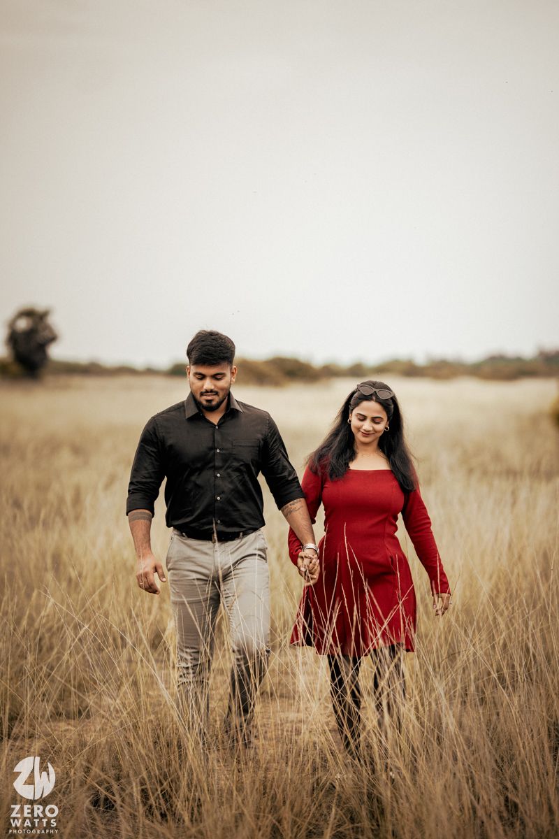 Couple walking hand in hand through tall golden grass at sunset.