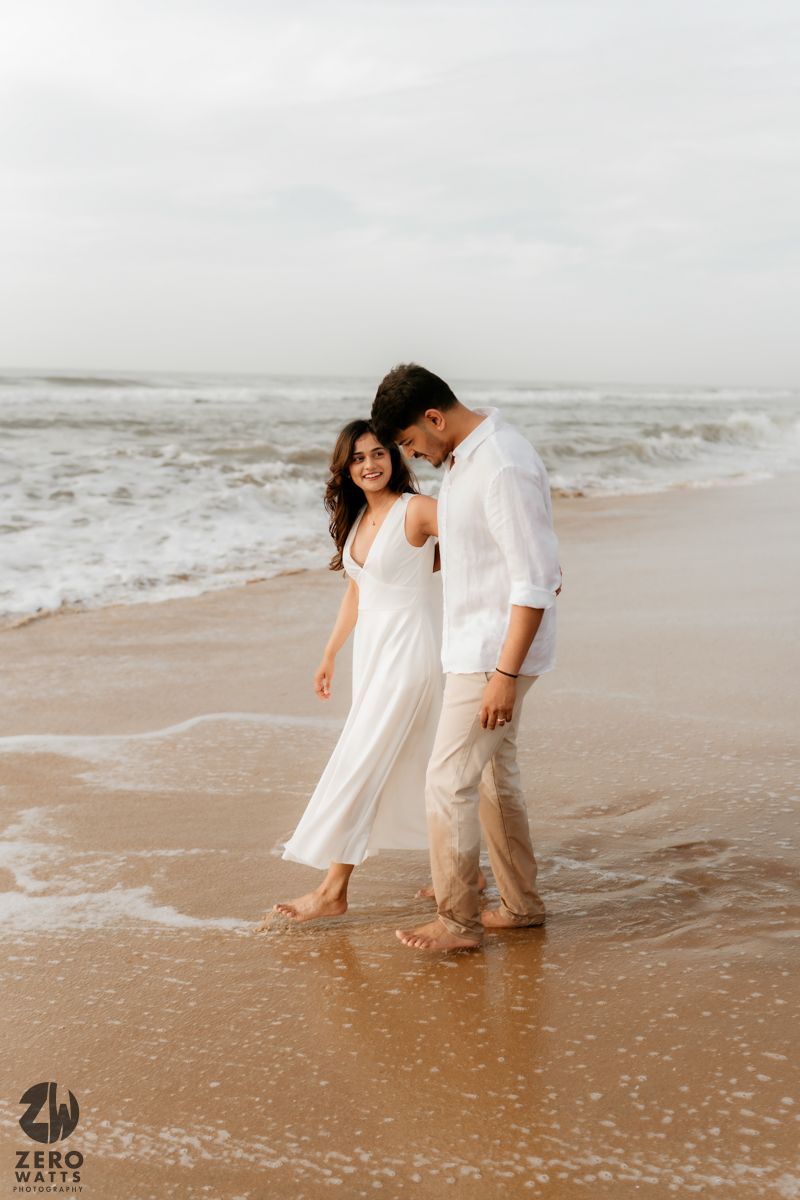A couple splashes and plays together in shallow ocean water at the beach.