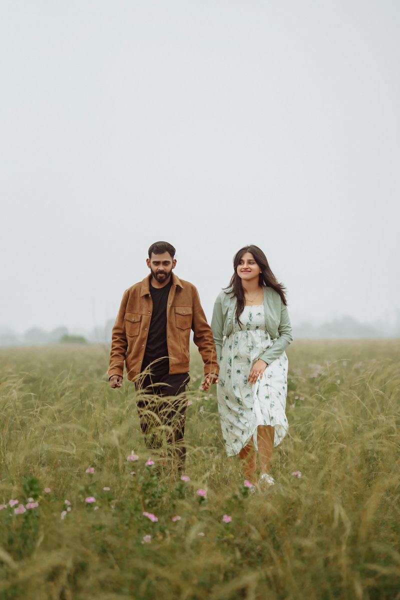 A couple walking hand in hand through a misty meadow with tall grass, wearing casual fall attire.