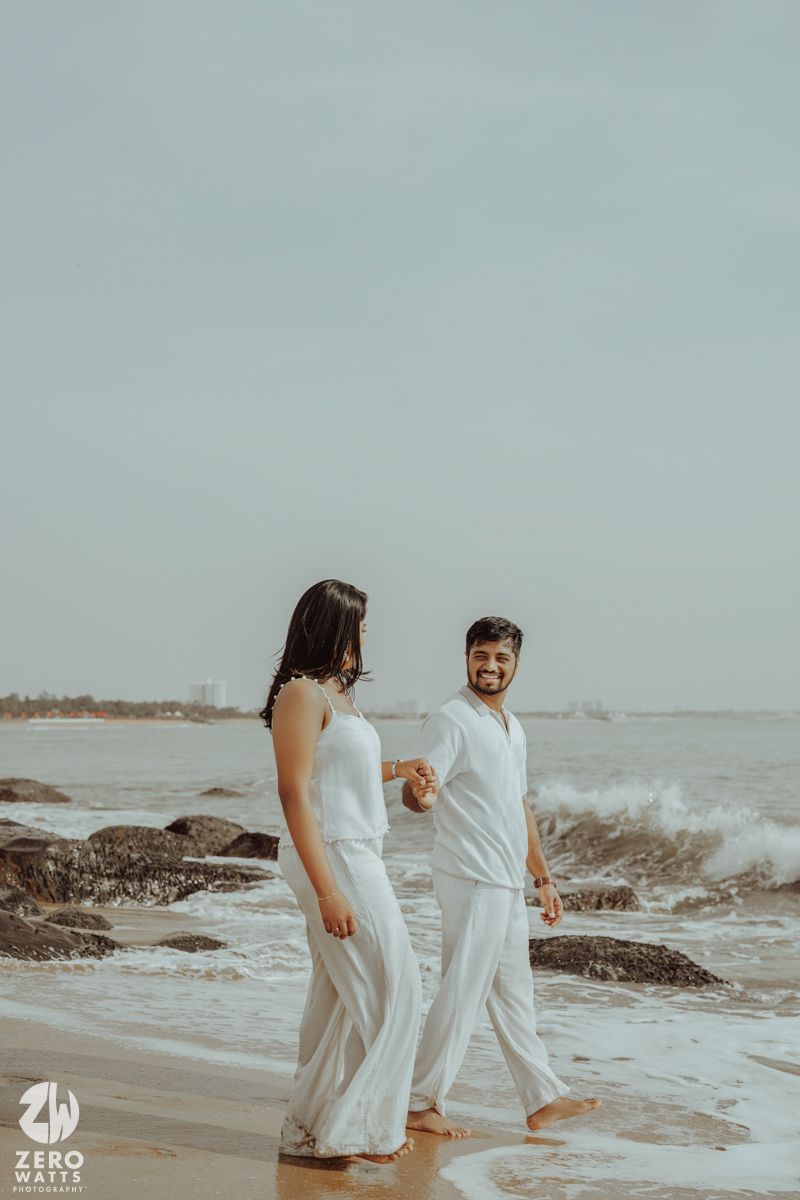 Couple sharing a moment while walking on rocky beach during overcast day.