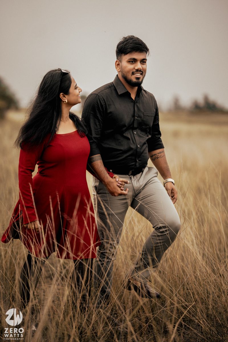 Couple walking together through tall grass wearing formal attire in warm evening light.