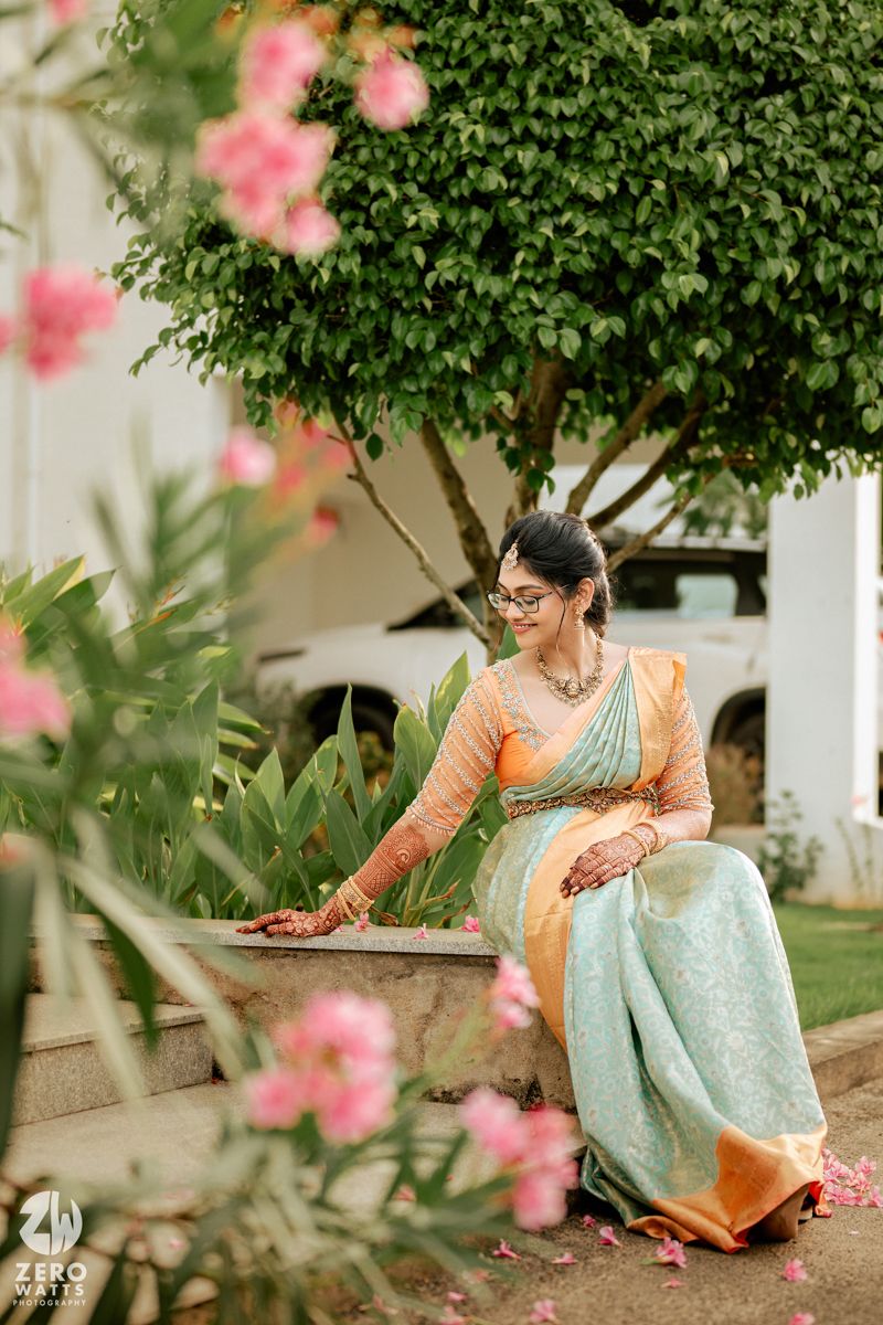 Beautiful silk saree in mint green and orange with intricate border design photographed in garden setting with pink flowers.