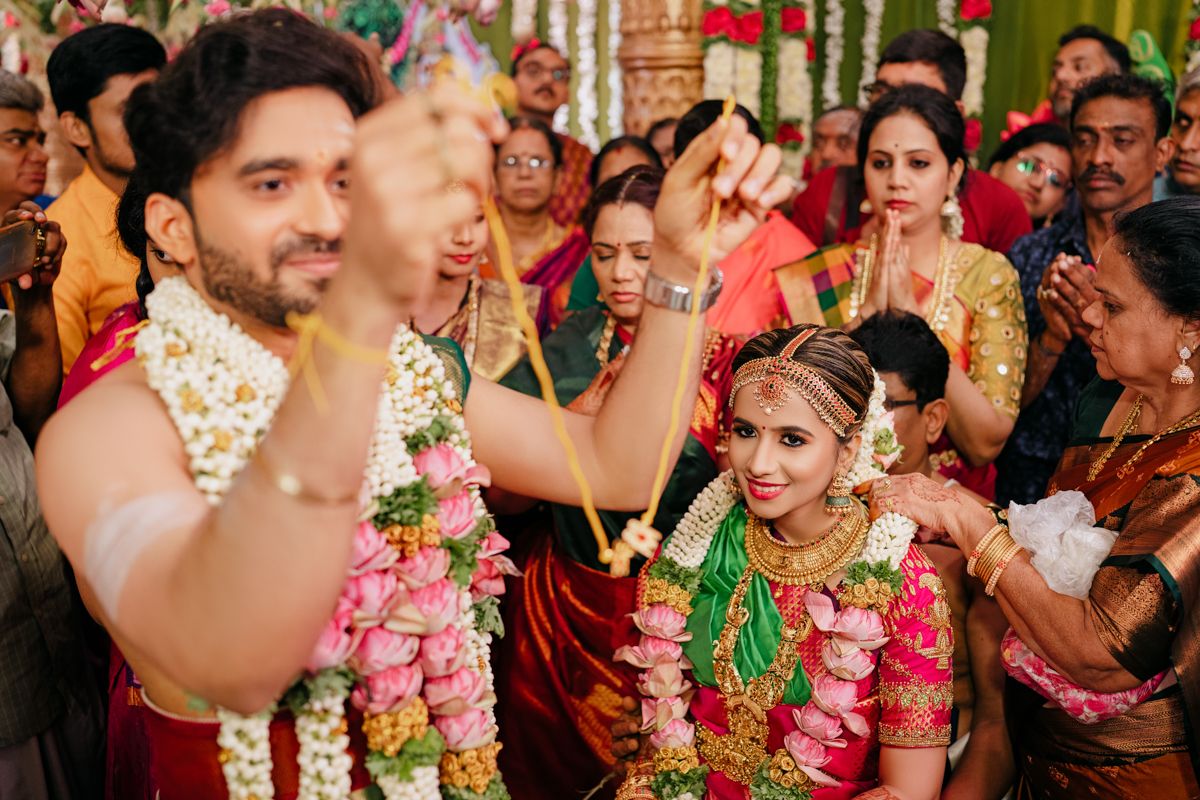 A couple in traditional Indian wedding attire celebrates with guests during a vibrant, colorful marriage ceremony.