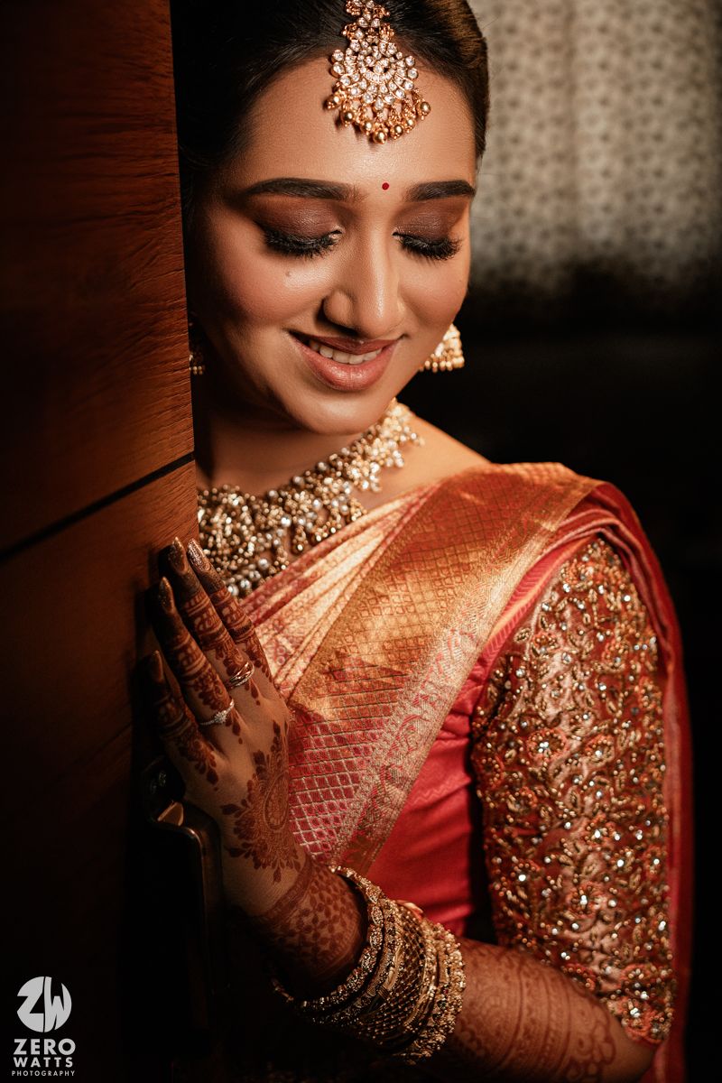 Traditional Indian bride wearing ornate gold jewelry, red silk saree and intricate mehndi designs on her hands in warm light.