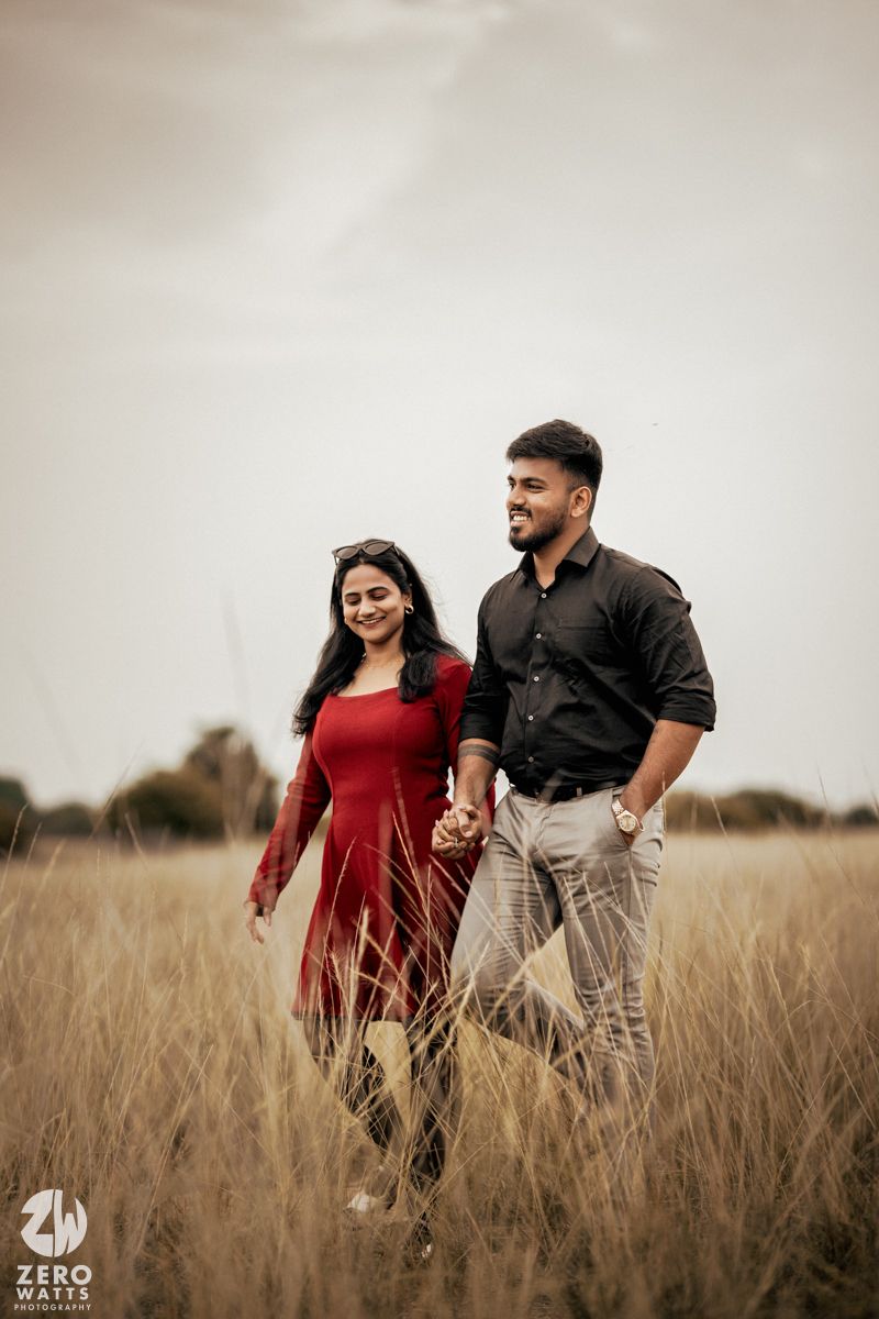 A couple walking hand in hand through a golden wheat field at sunset.