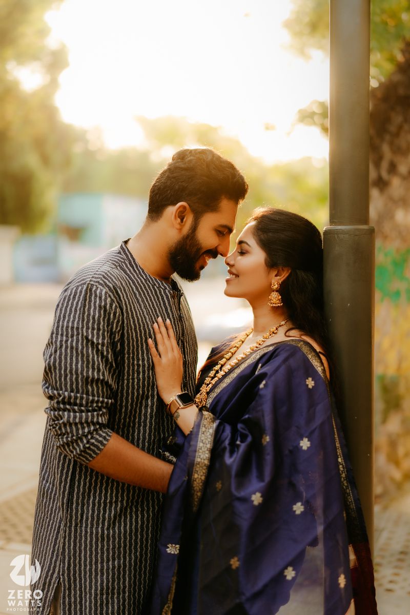 A couple in traditional Indian attire share a romantic moment at sunset against a blurred outdoor background.