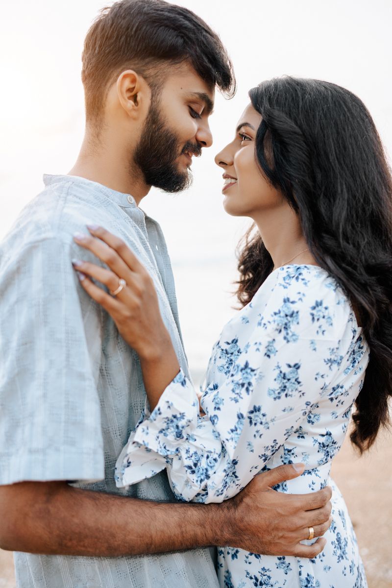 Intimate couple in blue and white outfits sharing tender moment against bright sky.