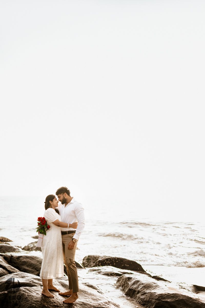 Romantic beach photoshoot with couple embracing on rocky shore.