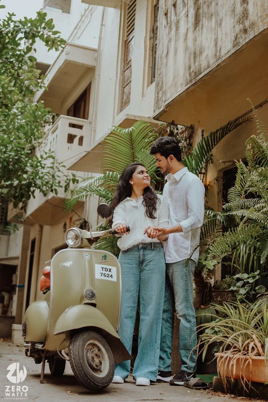 A cheerful couple posing with a mint-colored vintage Vespa scooter against a residential building.