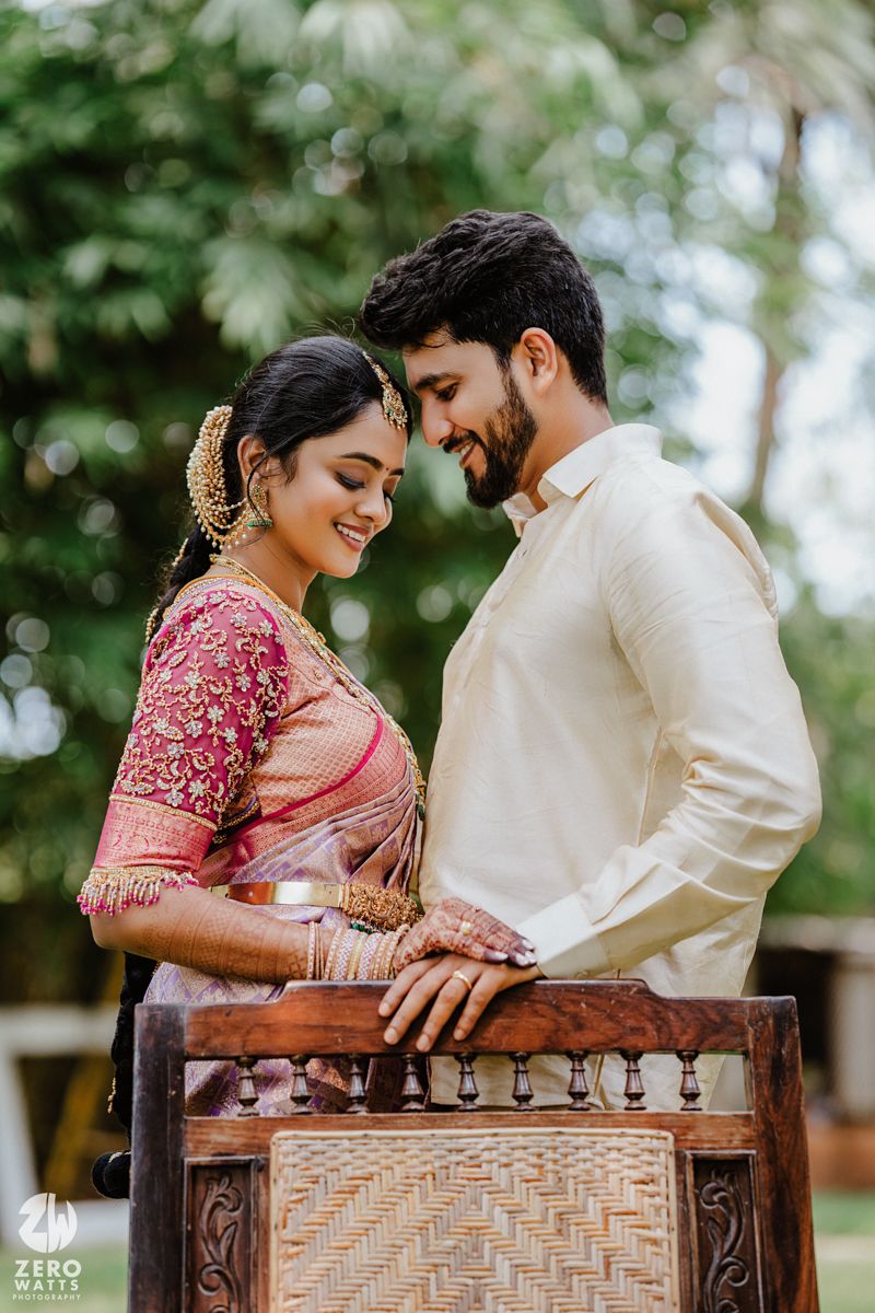 Romantic pose of couple in traditional South Indian wedding attire by wooden chair.