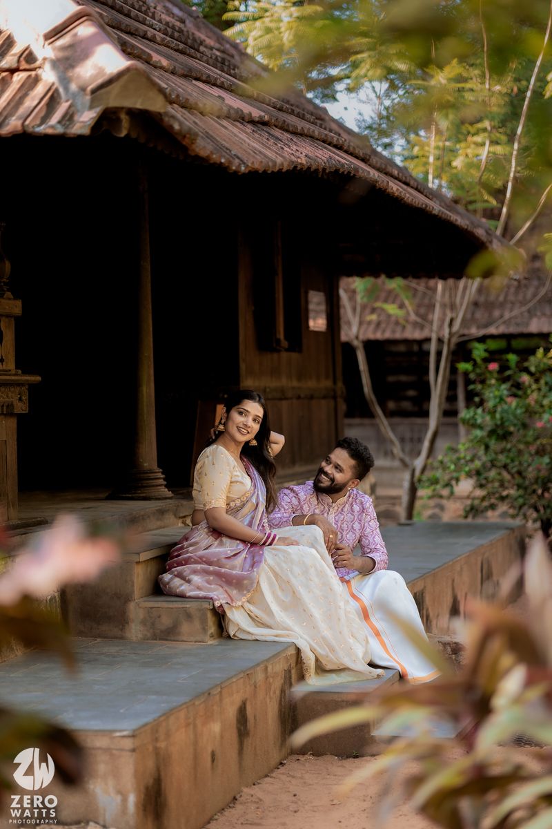 A couple shares an intimate moment on the porch of a traditional wooden cottage with thatched roof.