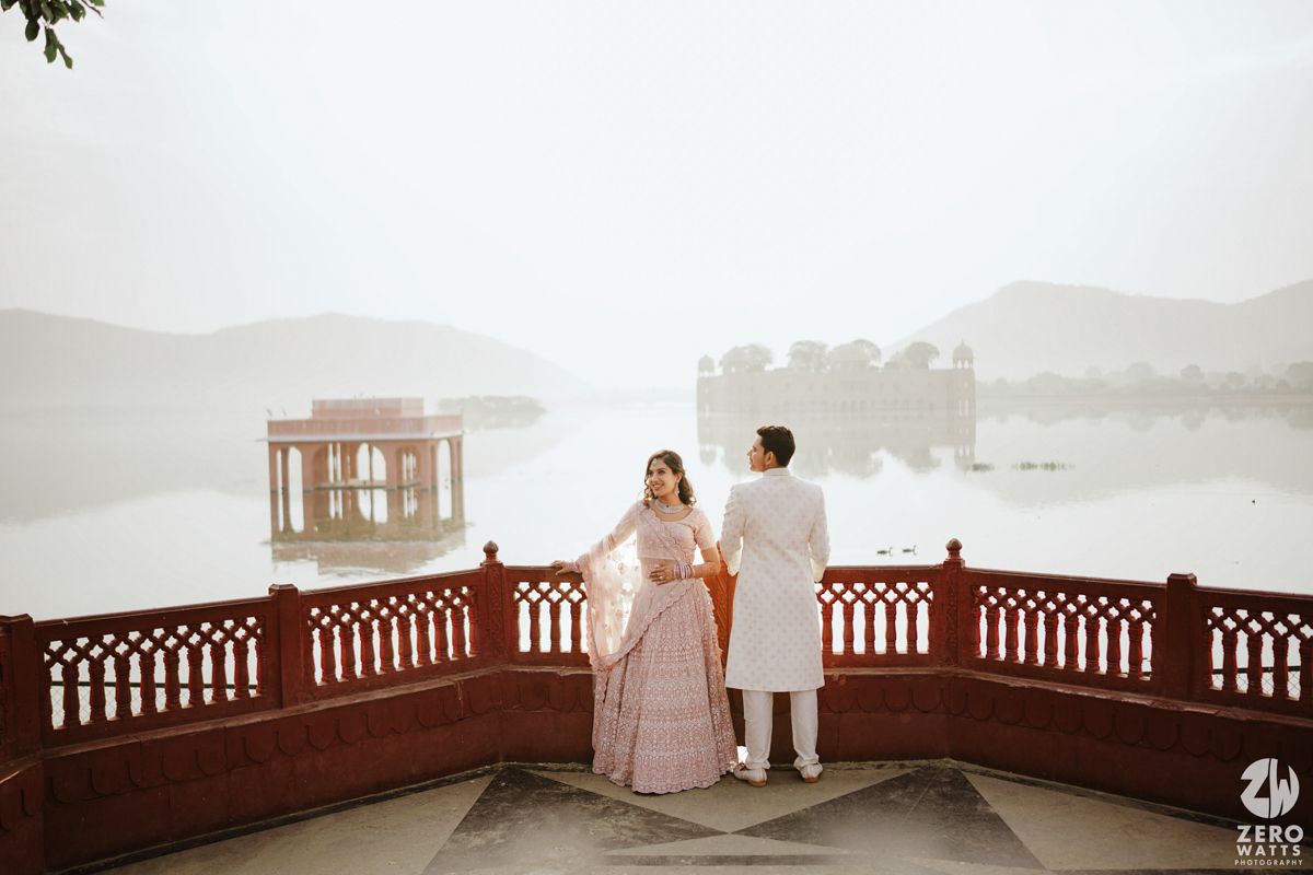 Black and white photo of a couple on a lakeside terrace with ornate railings and misty palace view.